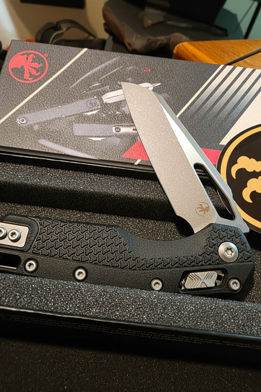 A folding pocket knife with a textured black handle and a satin silver blade, displayed inside its black presentation box with a branded red logo.