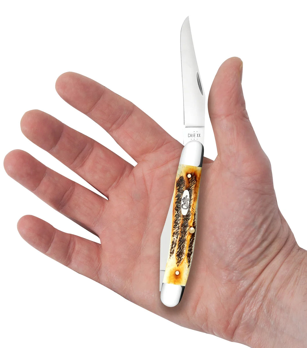 A pocket knife with a silver blade and a white handle featuring a brown and black animal skull inlay, held in an open hand against a white background.