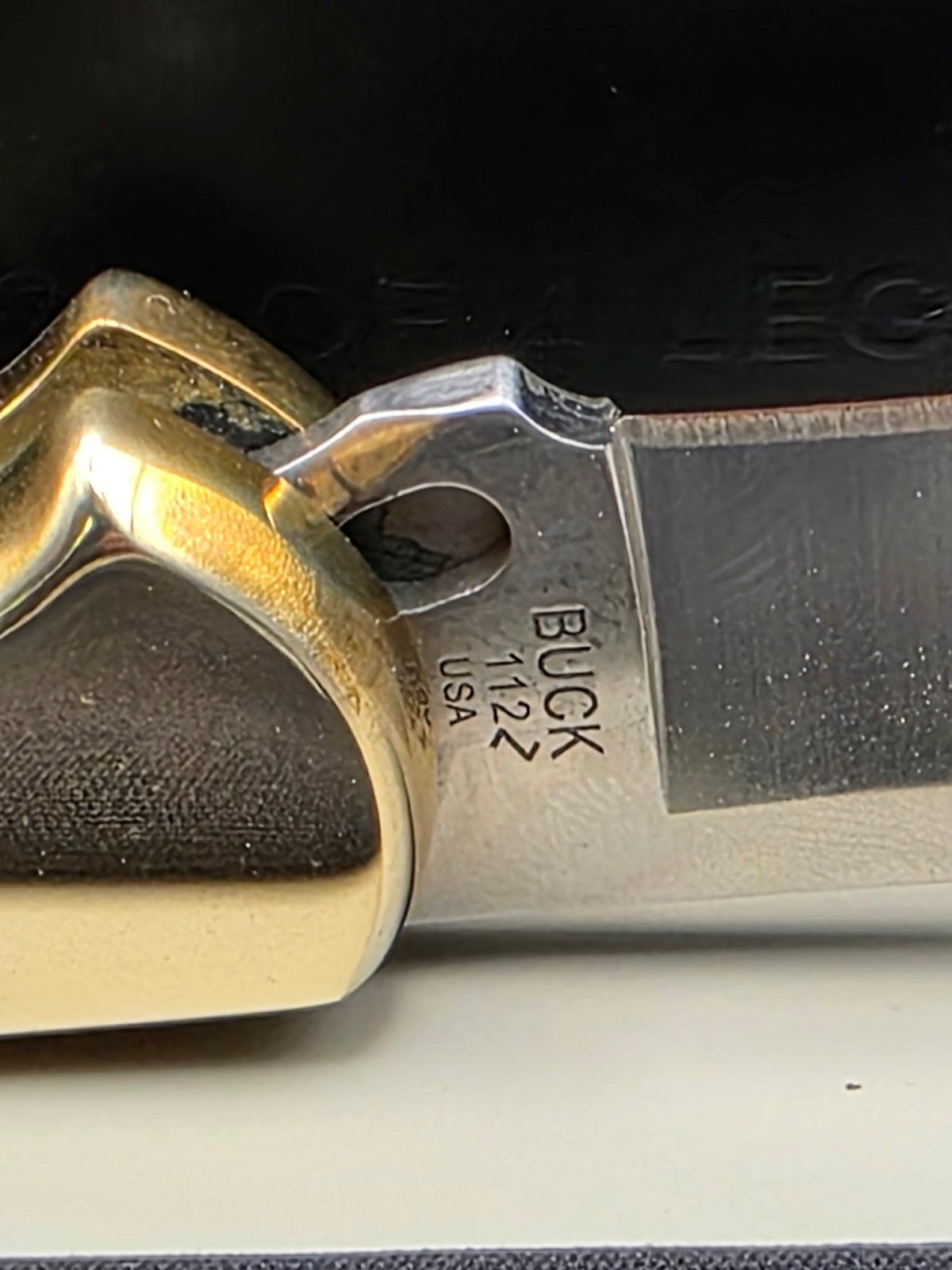 Close-up of a Buck 112 USA knife blade and handle, showing the metal blade with 'BUCK 112 USA' stamped on it and a brass-colored handle.