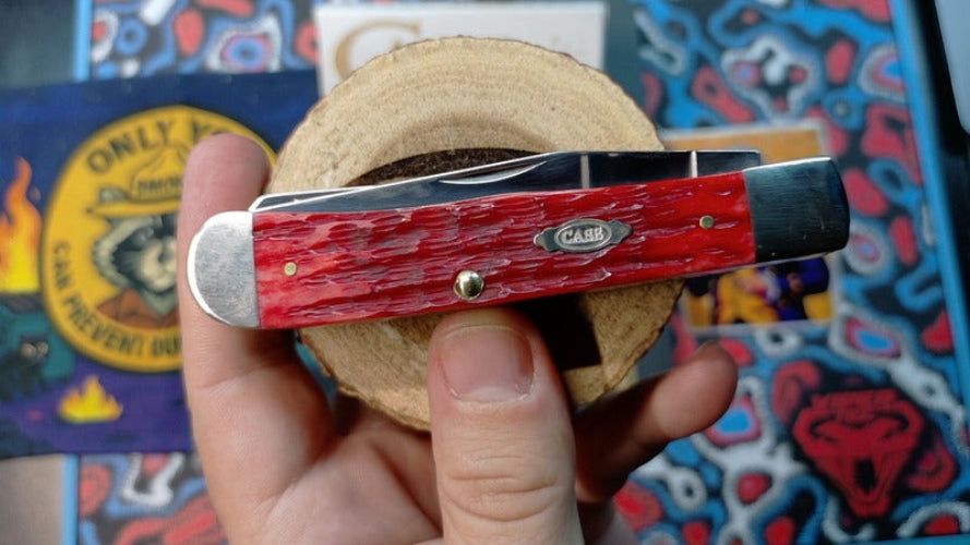 Red pocket knife held in a hand with a colorful background